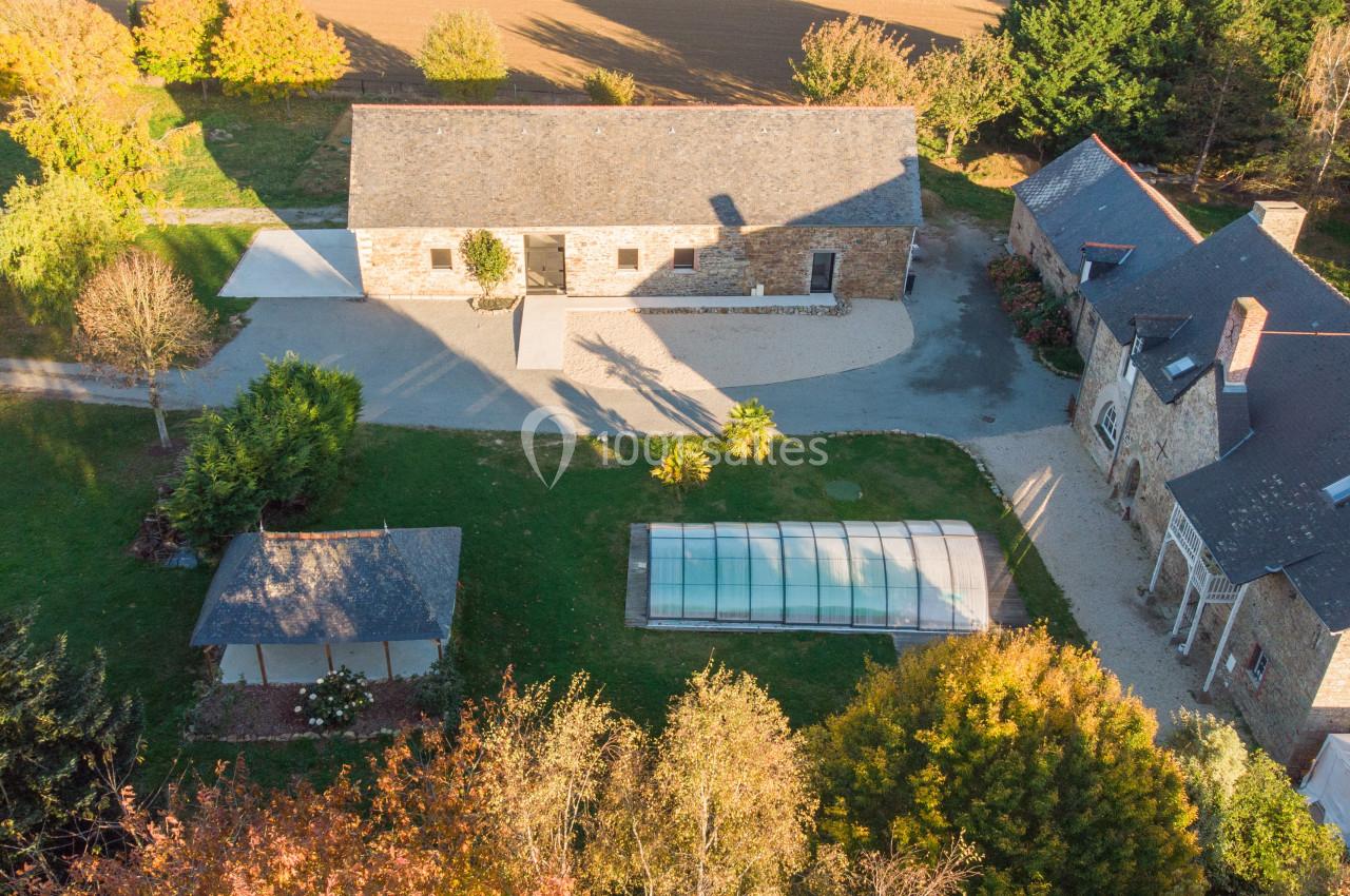 Vue aérienne d'une propriété avec bâtiments en pierre, piscine couverte et jardin arboré en automne.