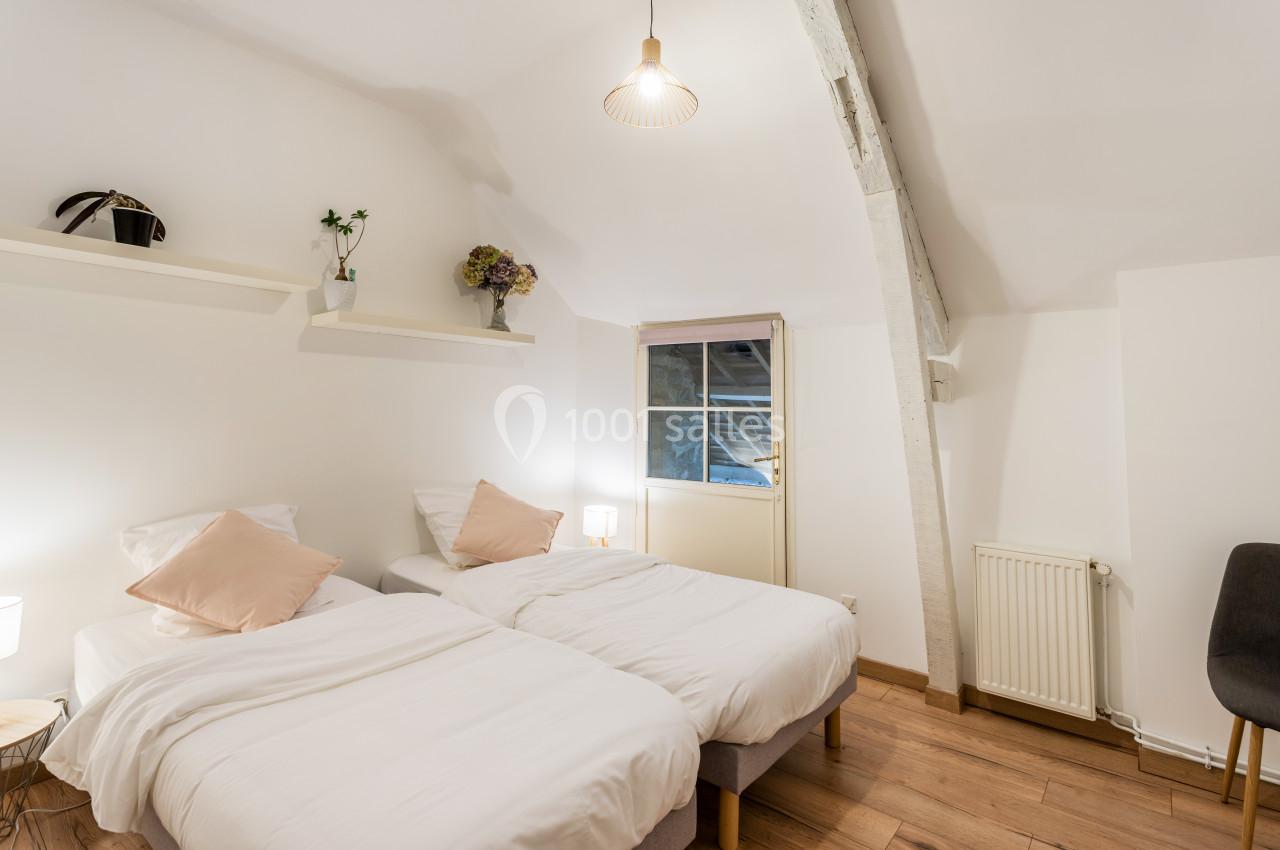 Deux lits simples avec draps blancs dans une chambre lumineuse, décorée de plantes et d'une fenêtre en arrière-plan.