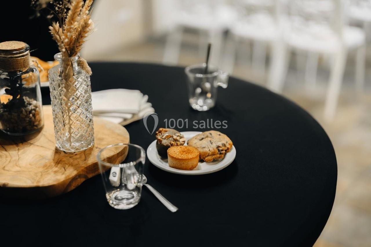 Assiette contenant des cookies et un petit gâteau sur une table noire, avec des verres et un vase décoratif à proximité.