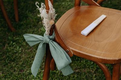 Un homme debout, bras ouverts, s'exprime devant un mur en pierre, avec une chaise en bois à côté de lui.