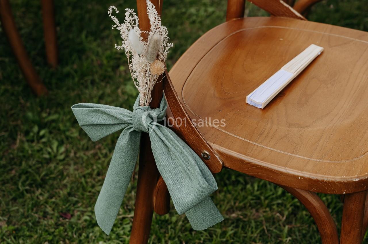 Chaise en bois décorée d'un ruban vert et d'un bouquet de fleurs séchées, placée sur une pelouse.