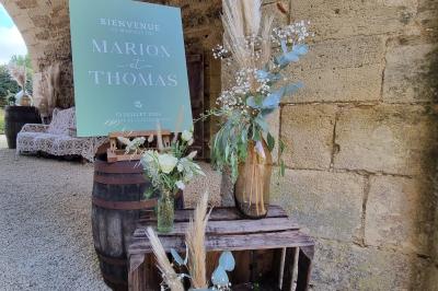 Un homme debout, bras ouverts, s'exprime devant un mur en pierre, avec une chaise en bois à côté de lui.