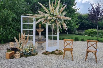Un homme debout, bras ouverts, s'exprime devant un mur en pierre, avec une chaise en bois à côté de lui.