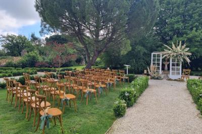 Un homme debout, bras ouverts, s'exprime devant un mur en pierre, avec une chaise en bois à côté de lui.