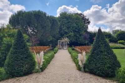 Un homme debout, bras ouverts, s'exprime devant un mur en pierre, avec une chaise en bois à côté de lui.