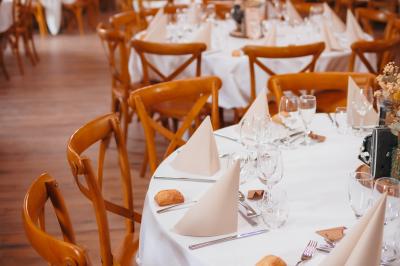 Un homme debout, bras ouverts, s'exprime devant un mur en pierre, avec une chaise en bois à côté de lui.