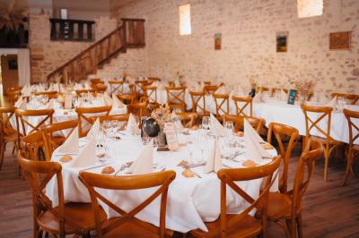 Un homme debout, bras ouverts, s'exprime devant un mur en pierre, avec une chaise en bois à côté de lui.
