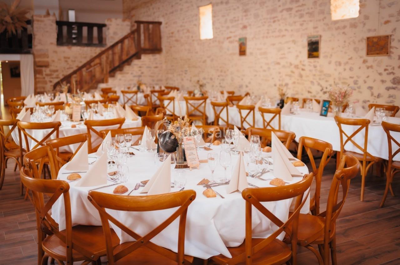 Salle de réception avec tables rondes dressées, nappes blanches, serviettes pliées et décorations florales.