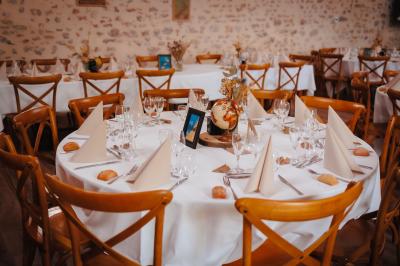 Un homme debout, bras ouverts, s'exprime devant un mur en pierre, avec une chaise en bois à côté de lui.