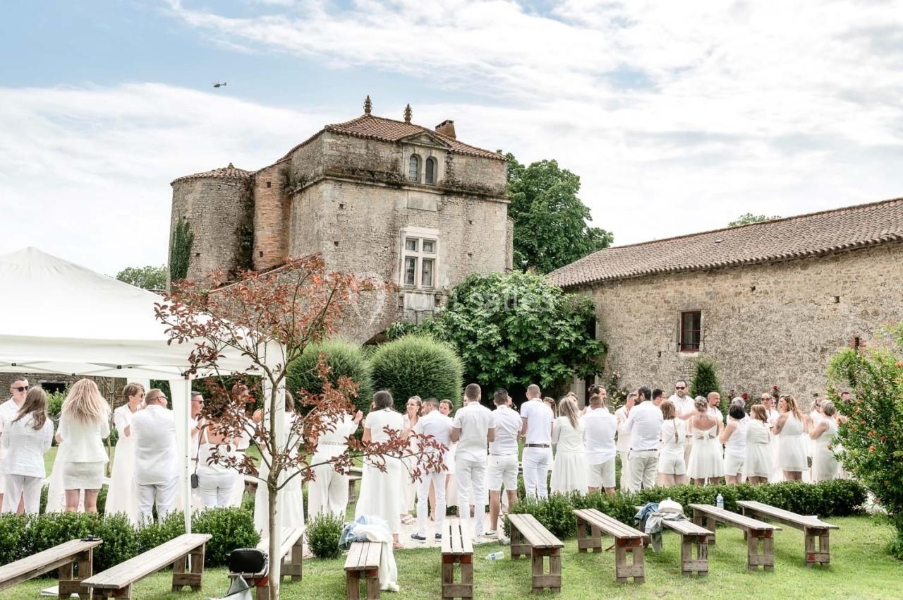 Groupe de personnes vêtues de blanc rassemblées dans un jardin devant un bâtiment en pierre historique.