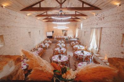 Un homme debout, bras ouverts, s'exprime devant un mur en pierre, avec une chaise en bois à côté de lui.