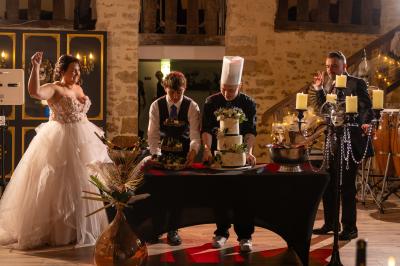 Un homme debout, bras ouverts, s'exprime devant un mur en pierre, avec une chaise en bois à côté de lui.