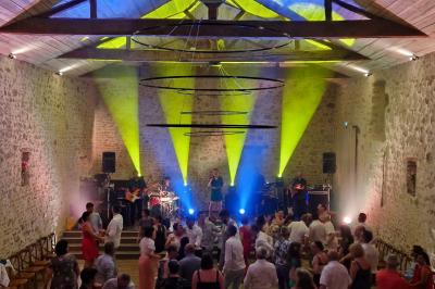 Un homme debout, bras ouverts, s'exprime devant un mur en pierre, avec une chaise en bois à côté de lui.