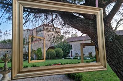 Un homme debout, bras ouverts, s'exprime devant un mur en pierre, avec une chaise en bois à côté de lui.