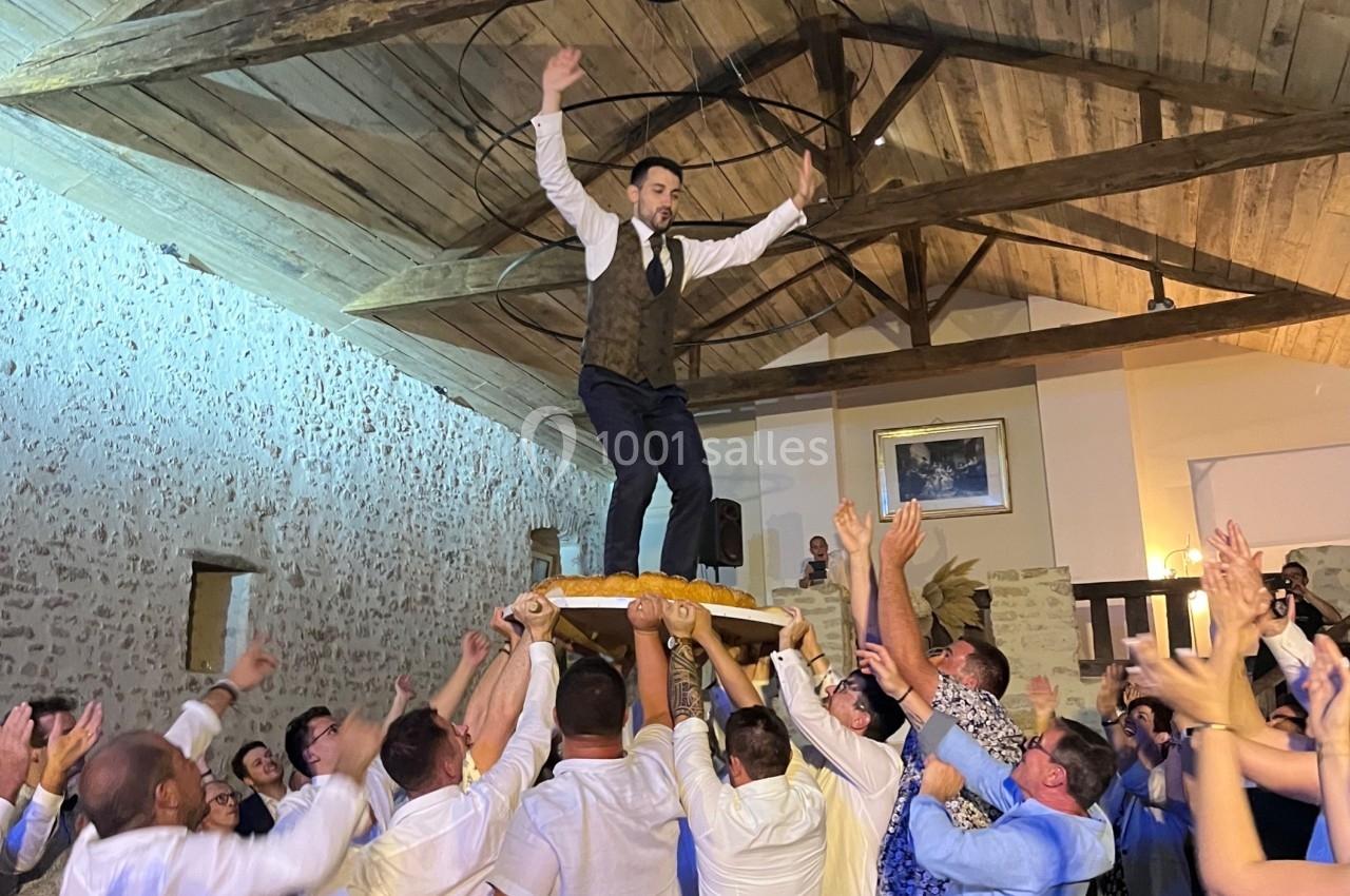 Un homme debout sur une chaise portée par une foule dans une salle avec un plafond en bois.