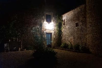 Un homme debout, bras ouverts, s'exprime devant un mur en pierre, avec une chaise en bois à côté de lui.