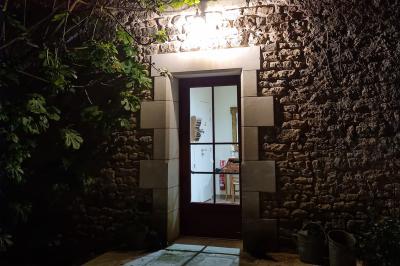 Un homme debout, bras ouverts, s'exprime devant un mur en pierre, avec une chaise en bois à côté de lui.