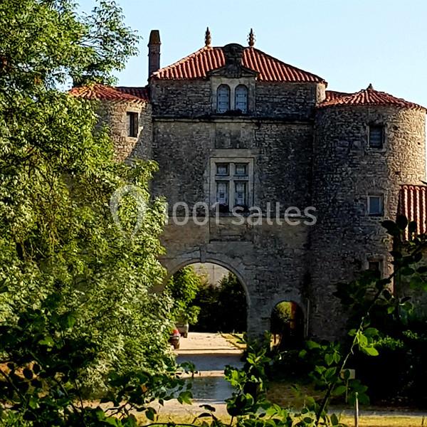 Vue d'une entrée voûtée en pierre d'un bâtiment historique entouré de verdure.