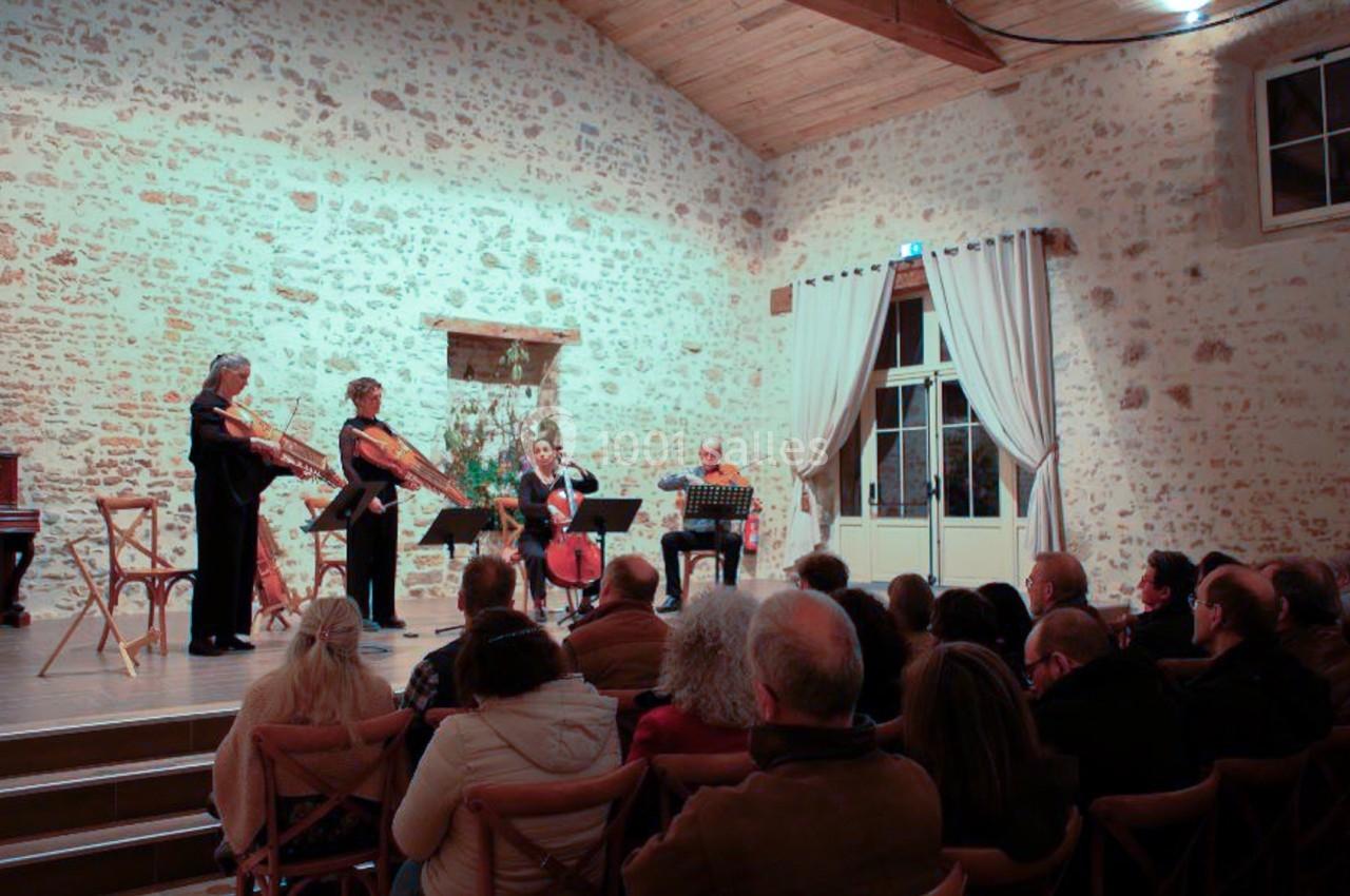 Un quatuor à cordes joue devant un public dans une salle en pierre avec un plafond en bois.