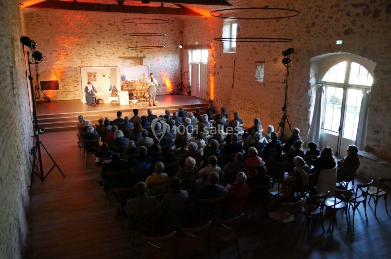 Un public assis dans une salle en pierre avec une scène éclairée où des personnes jouent une pièce de théâtre.
