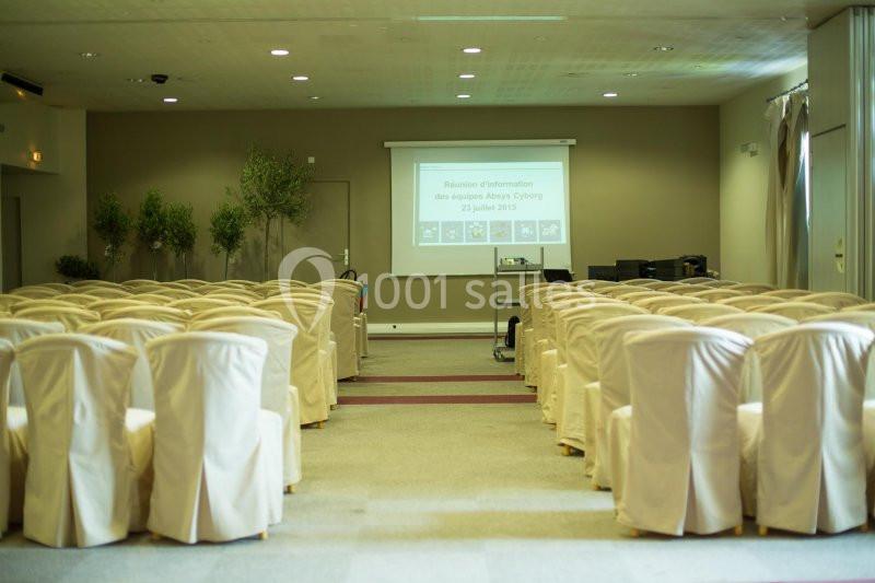 Salle de conférence vide avec des rangées de chaises blanches et un écran de projection affichant une présentation.