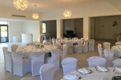 Bâtiment en pierre de style méditerranéen entouré d'arbres, avec une terrasse et une pelouse au premier plan.