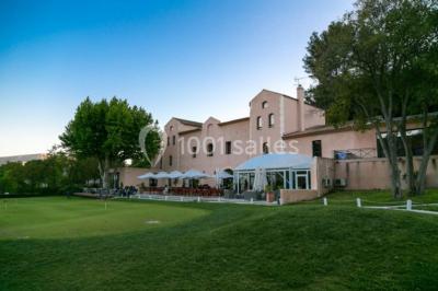 Bâtiment en pierre de style méditerranéen entouré d'arbres, avec une terrasse et une pelouse au premier plan.