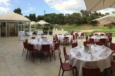 Bâtiment en pierre de style méditerranéen entouré d'arbres, avec une terrasse et une pelouse au premier plan.