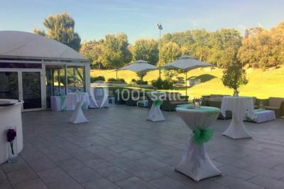 Bâtiment en pierre de style méditerranéen entouré d'arbres, avec une terrasse et une pelouse au premier plan.