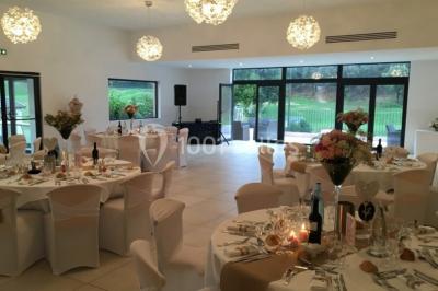 Bâtiment en pierre de style méditerranéen entouré d'arbres, avec une terrasse et une pelouse au premier plan.