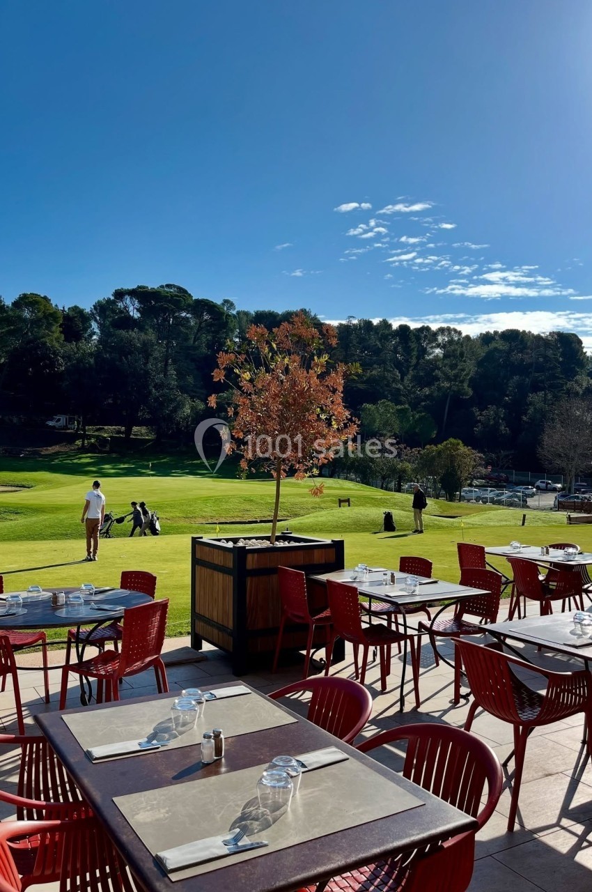 Location salle Marseille 11 (Bouches-du-Rhône) - La Bastide de la Salette #3 Terrasse d'un restaurant avec des tables vides, vue sur un terrain de golf entouré d'arbres sous un ciel ensoleillé.