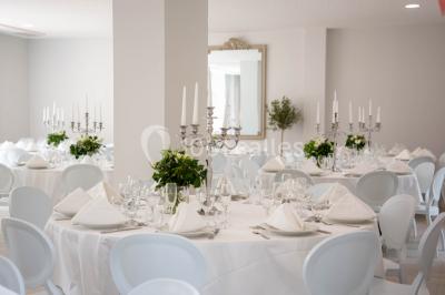 Salle de réception décorée avec des tables rondes recouvertes de nappes rouges, ornées de compositions florales.