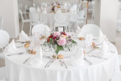 Salle de réception décorée avec des tables rondes recouvertes de nappes rouges, ornées de compositions florales.