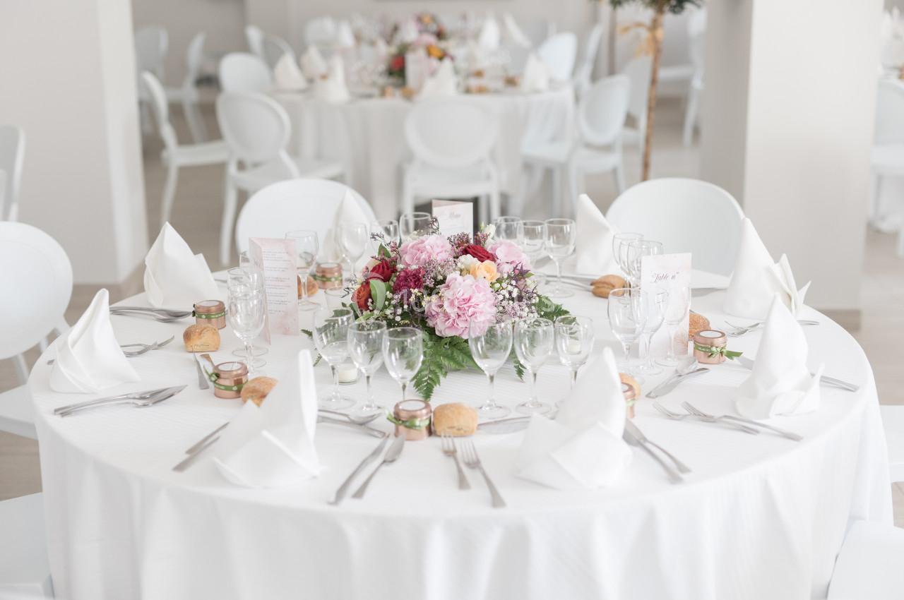 Table de réception élégamment dressée avec nappes blanches, bouquet floral central, verres et couverts disposés.
