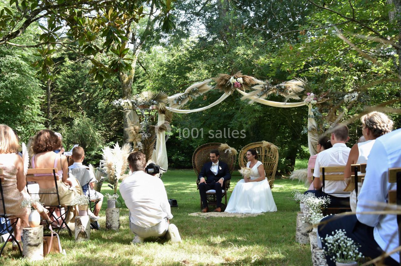 Cérémonie de mariage en plein air avec des invités assis, un couple marié sous une arche décorée dans un cadre verdoyant.