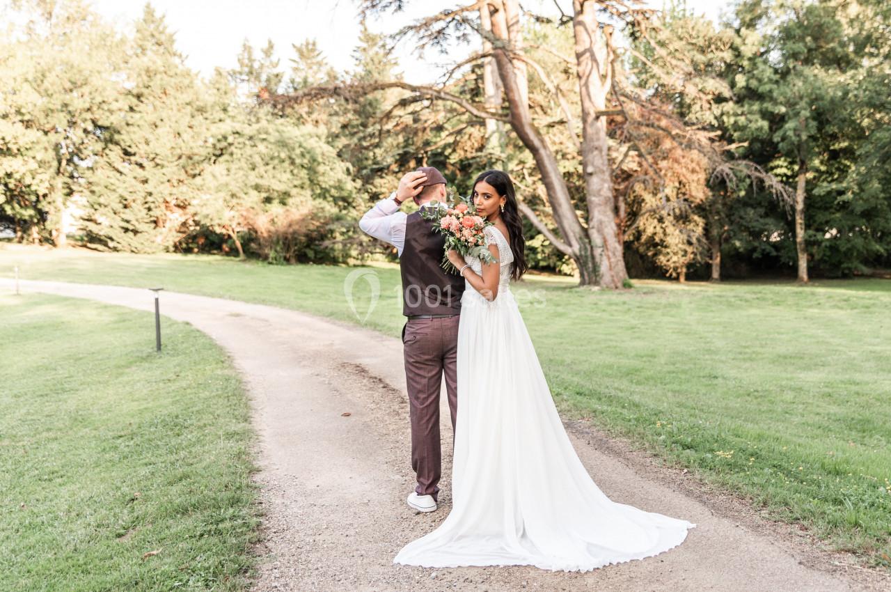 Un couple de mariés pose sur un chemin bordé de verdure, la mariée tenant un bouquet de fleurs.
