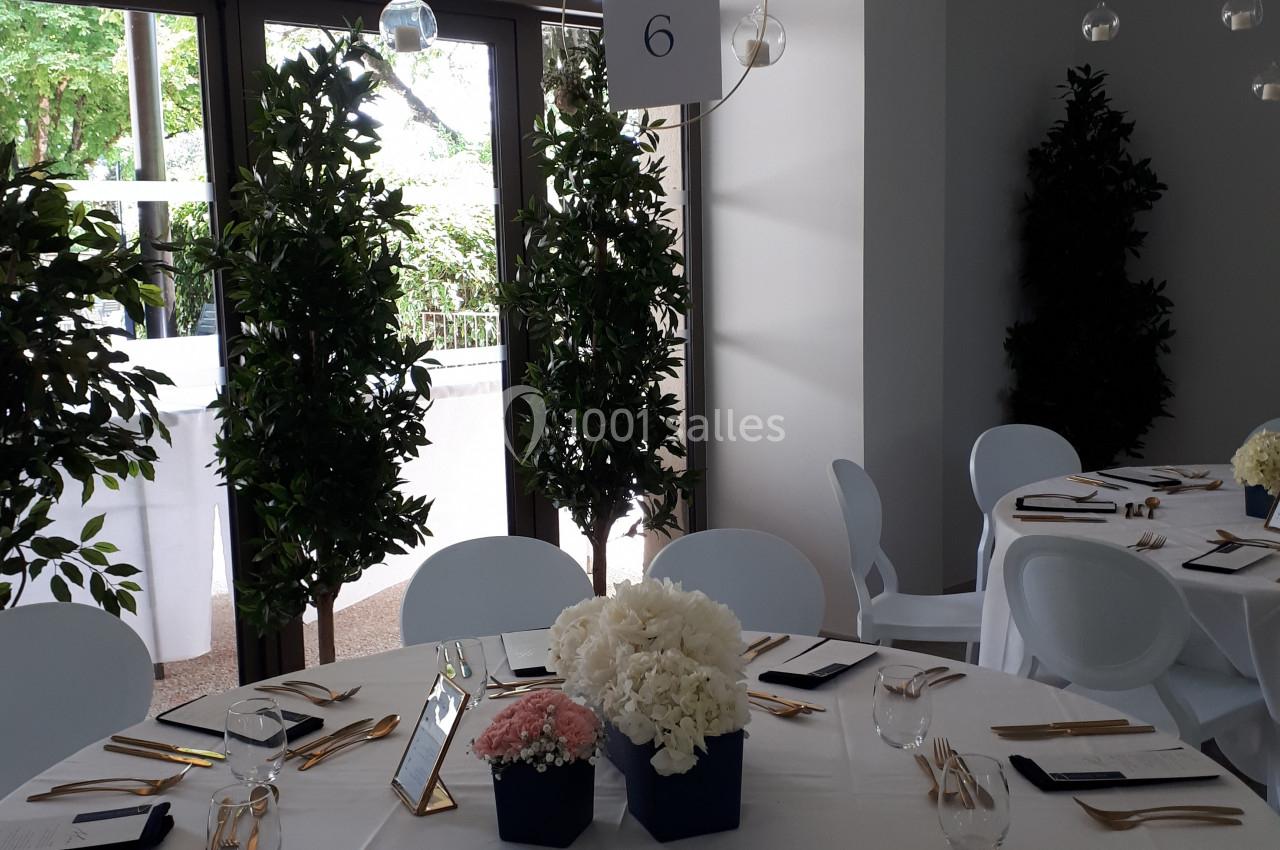 Salle de réception avec table ronde dressée, couverts dorés, centre de table floral et panneau indiquant ’Table 6’.