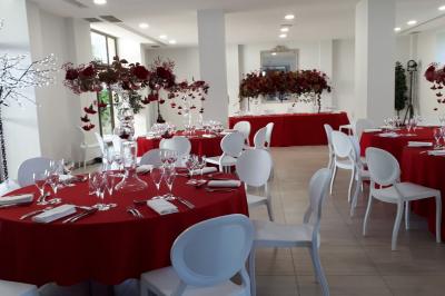 Salle de réception décorée avec des tables rondes recouvertes de nappes rouges, ornées de compositions florales.