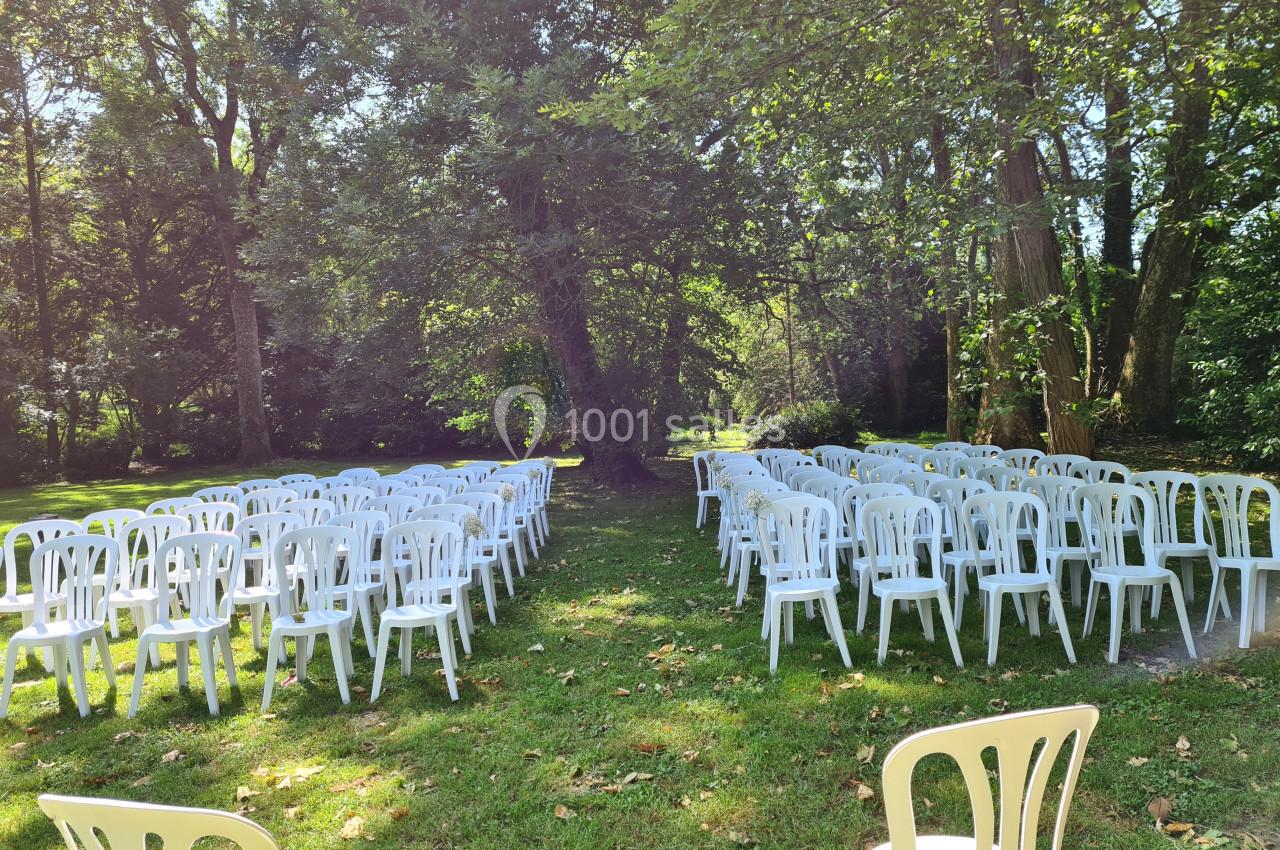 Chaises blanches disposées en rangées sur une pelouse, entourées d'arbres dans un cadre extérieur ensoleillé.
