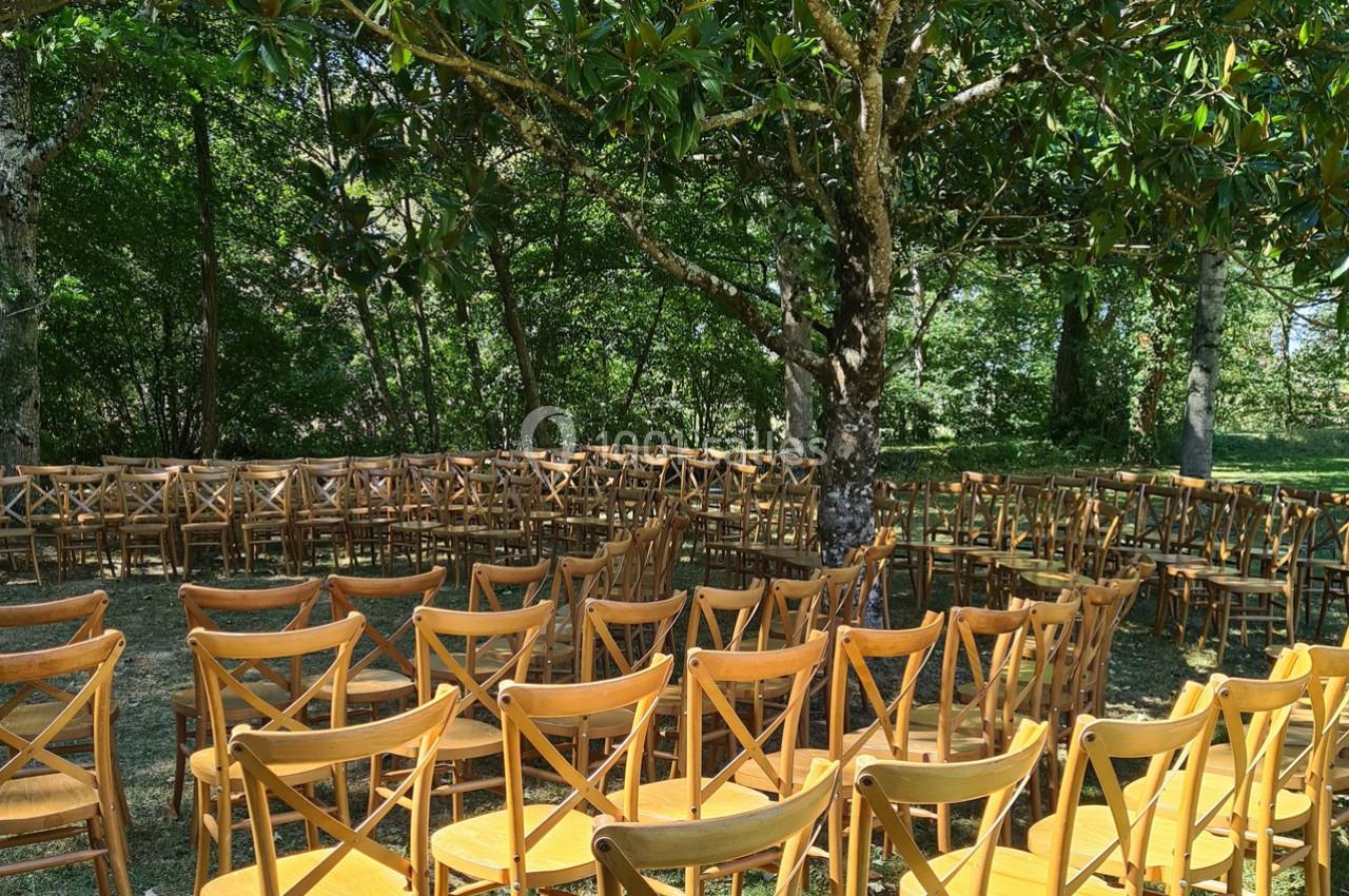 Chaises en bois disposées en cercle sous des arbres dans un espace extérieur ombragé.