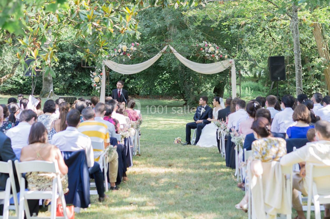 Cérémonie de mariage en plein air avec des invités assis, un couple au centre et un officiant sous une arche décorée.