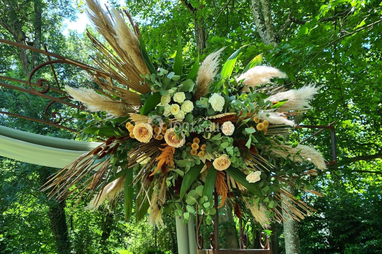 Composition florale suspendue avec des roses, des herbes de la pampa et des feuillages, dans un cadre naturel verdoyant.