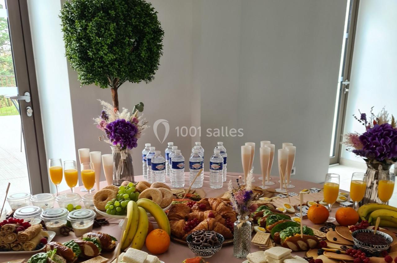 Table garnie de viennoiseries, fruits, sandwichs, jus d'orange, bouteilles d'eau et décorations florales.