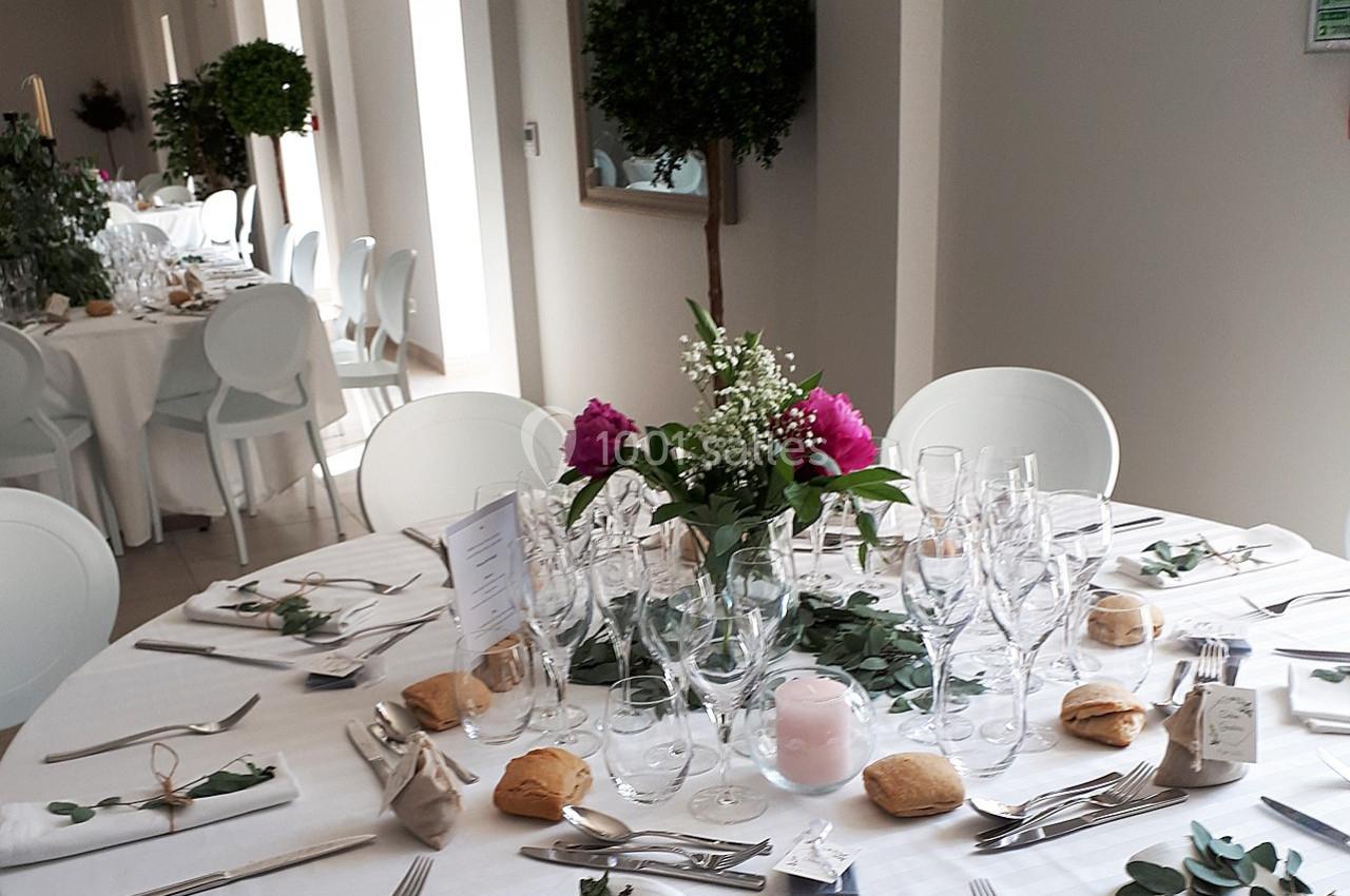 Table élégamment dressée pour un repas, avec vaisselle, fleurs, bougies et petits pains, dans une salle lumineuse.