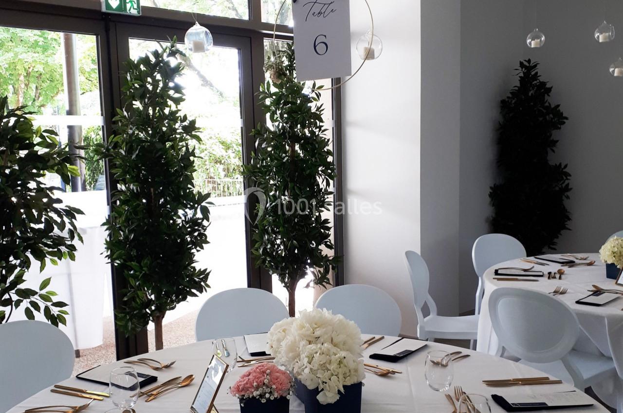 Table décorée pour un événement avec nappes blanches, fleurs, couverts dorés et panneau indiquant ’Table 6’.