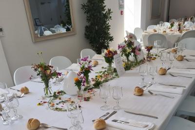 Salle de réception décorée avec des tables rondes recouvertes de nappes rouges, ornées de compositions florales.