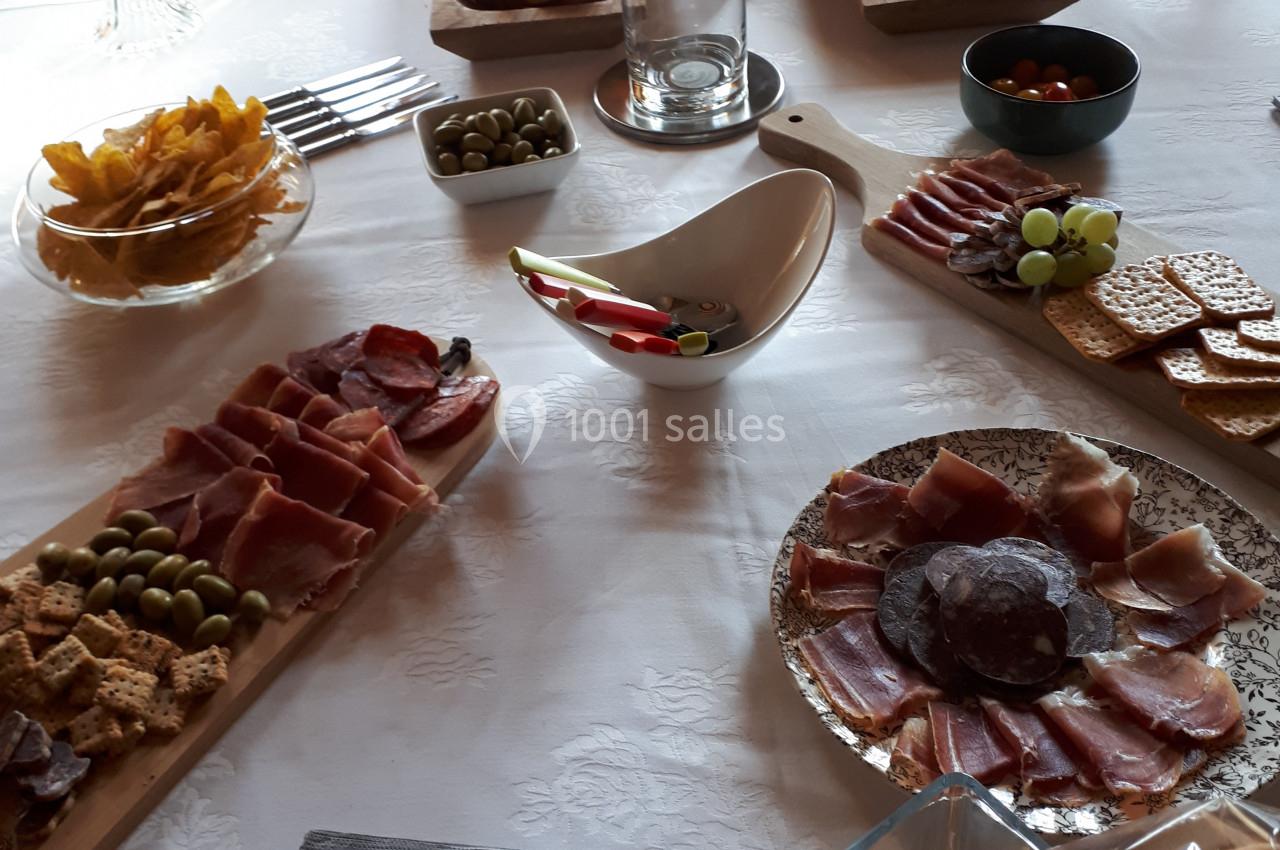 Table dressée avec des plateaux de charcuterie, fromages, olives, biscuits apéritifs et un bouquet de fleurs au centre.