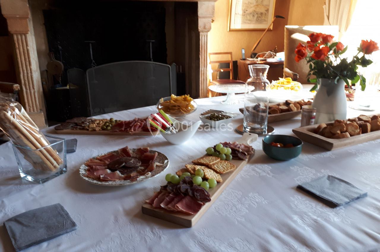 Table dressée avec des plateaux de charcuterie, fromages, fruits, pains et grissini, dans une salle à manger chaleureuse.