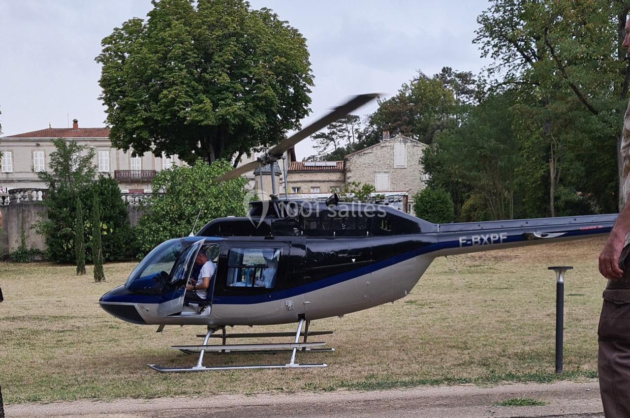 Un hélicoptère posé sur une pelouse près d'arbres et de bâtiments, avec une personne à bord.
