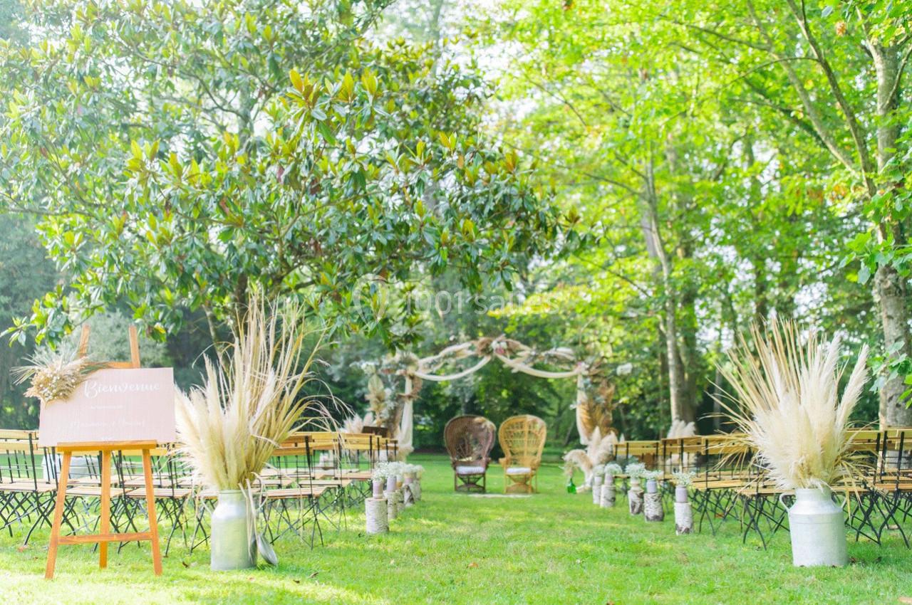 Allée décorée pour une cérémonie en plein air, avec chaises alignées, arches fleuries et végétation verdoyante.